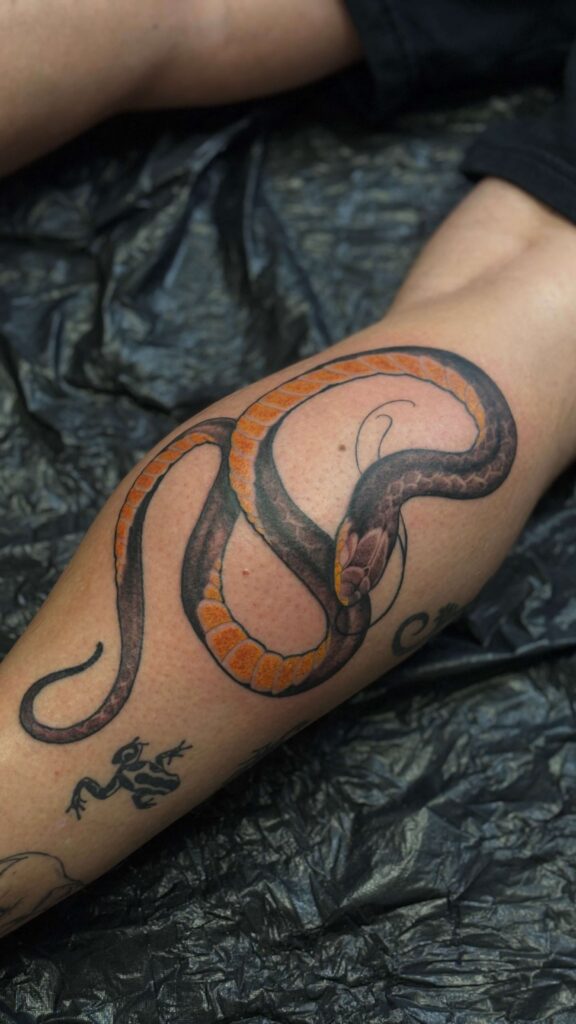 Tatovering med slange og orange farvedetaljer på underben – Timeless Studio Roskilde